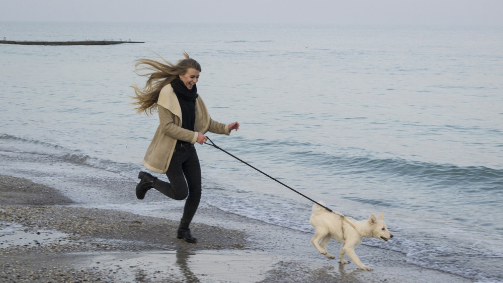 Nő fut a vízparton a kutyájával