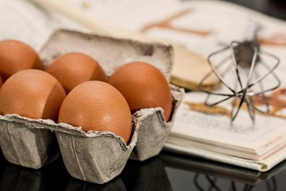 tojások tojástartóban, mellettük receptkönyv, rajta habverő